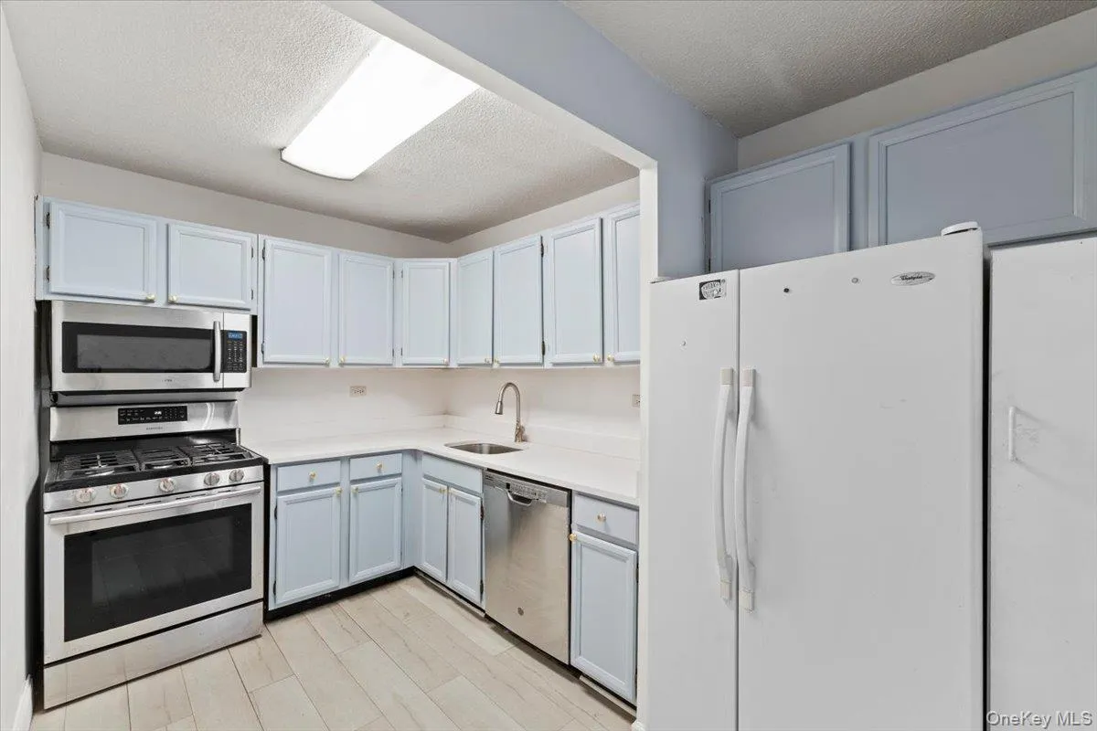 Kitchen featuring appliances with stainless steel finishes, a textured ceiling, light wood-type flooring, and gray cabinetry Kitchen featuring appliances with stainless steel finishes, a textured ceiling, light wood-type flooring, and gray cabinetry