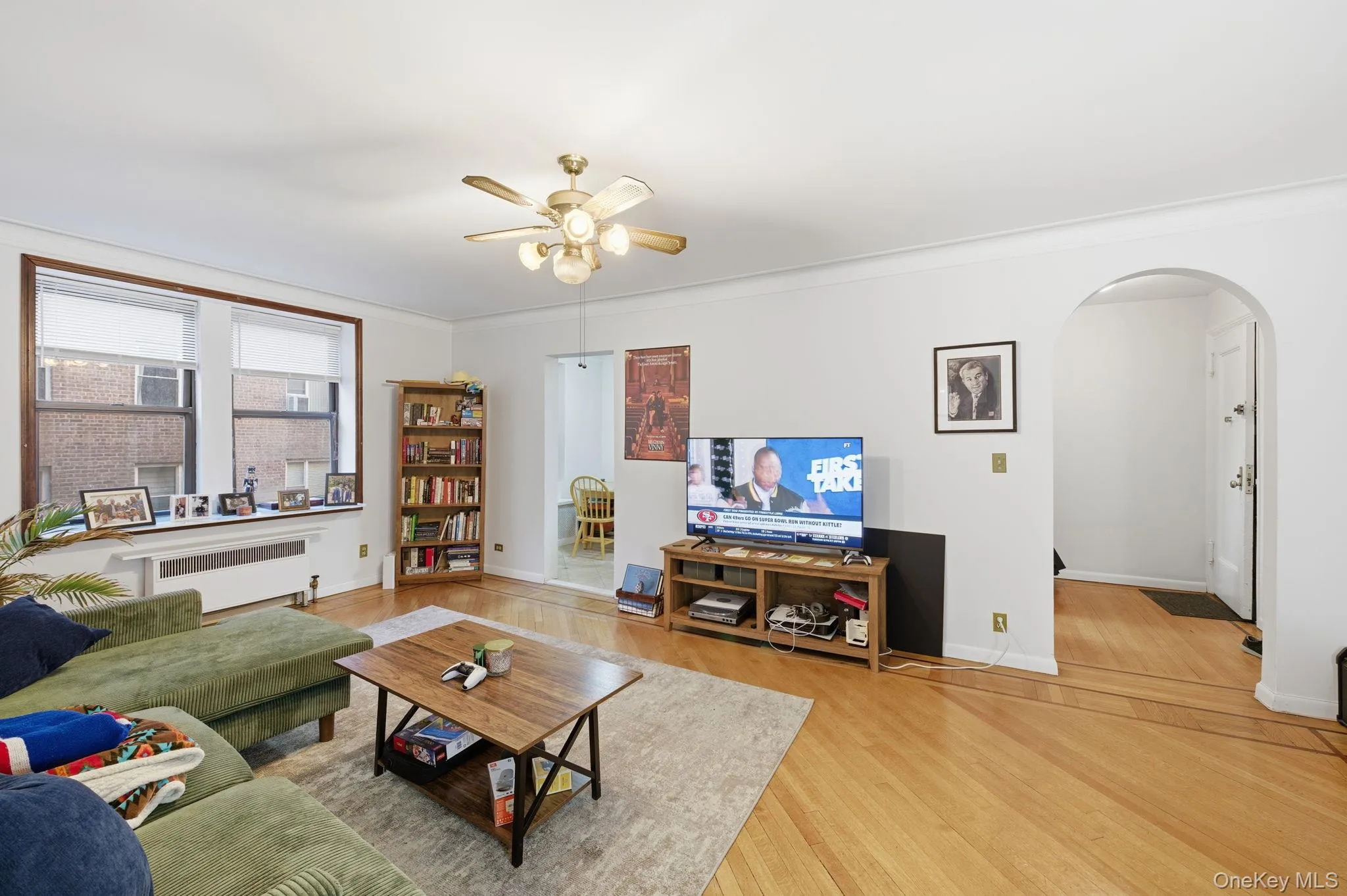 Living room featuring arched walkways, radiator heating unit, wood finished floors, crown molding, and ceiling fan Living room featuring arched walkways, radiator heating unit, wood finished floors, crown molding, and ceiling fan