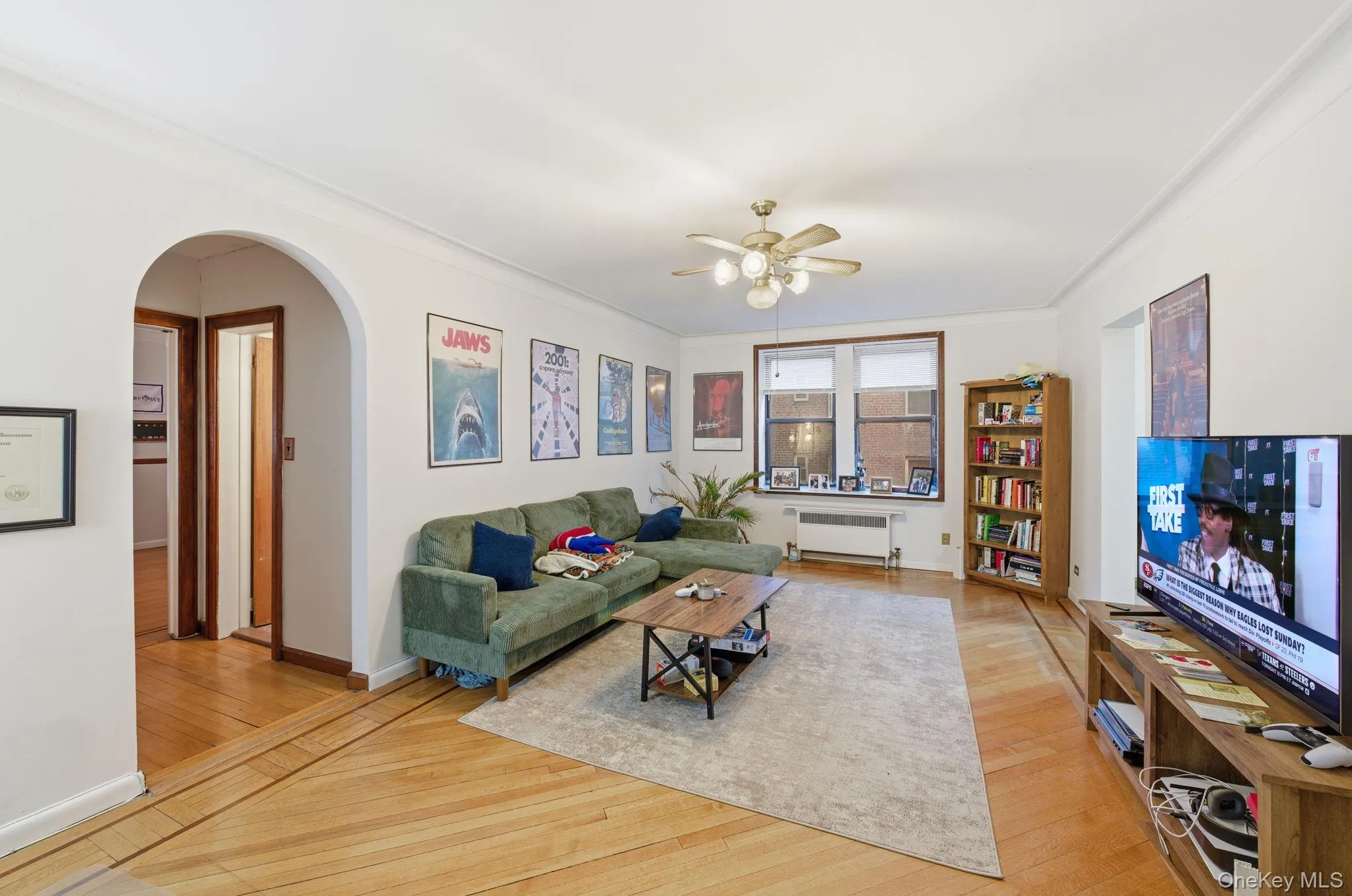 Living room featuring arched walkways, light wood finished floors, crown molding, radiator heating unit, and a ceiling fan Living room featuring arched walkways, light wood finished floors, crown molding, radiator heating unit, and a ceiling fan