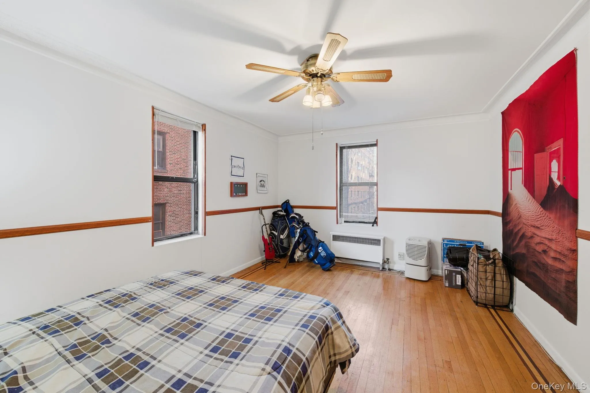 Bedroom featuring light wood finished floors, ceiling fan, radiator heating unit, ornamental molding, and multiple windows Bedroom featuring light wood finished floors, ceiling fan, radiator heating unit, ornamental molding, and multiple windows