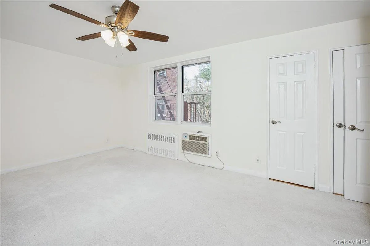 Carpeted empty room with radiator heating unit, a ceiling fan, and a wall mounted AC Carpeted empty room with radiator heating unit, a ceiling fan, and a wall mounted AC