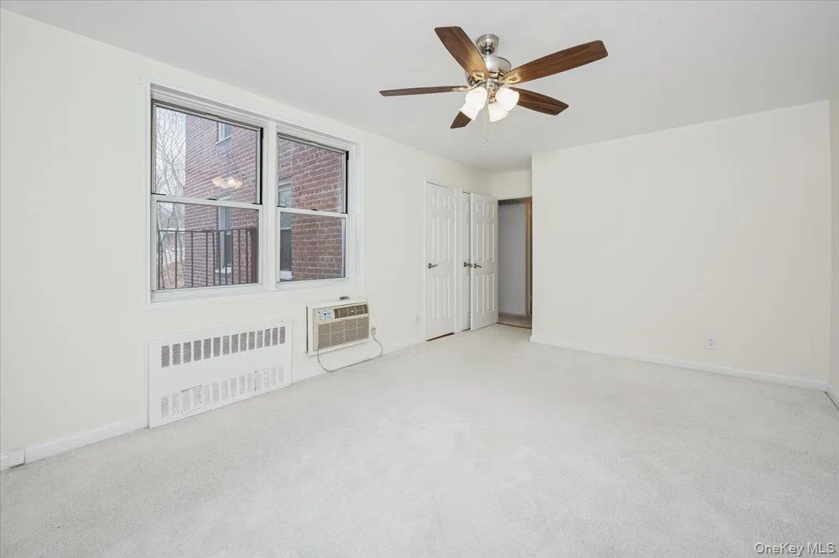 Unfurnished bedroom with radiator heating unit, ceiling fan, light colored carpet, and a wall unit AC Unfurnished bedroom with radiator heating unit, ceiling fan, light colored carpet, and a wall unit AC
