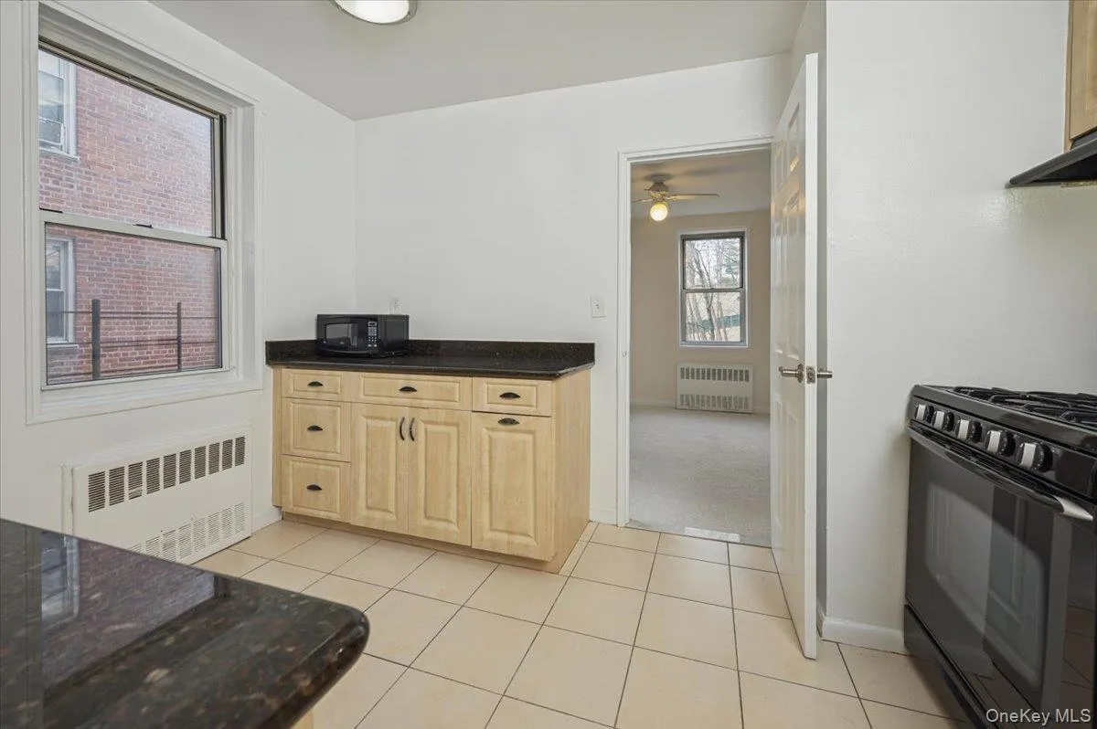 Kitchen featuring black appliances, radiator heating unit, dark stone counters, and light brown cabinetry Kitchen featuring black appliances, radiator heating unit, dark stone counters, and light brown cabinetry