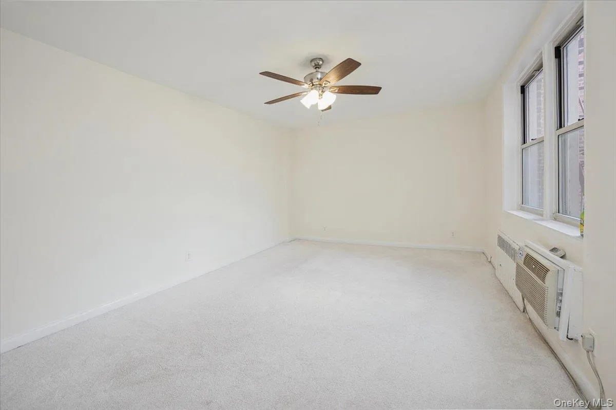 Empty room featuring light carpet, ceiling fan, and a wall unit AC Empty room featuring light carpet, ceiling fan, and a wall unit AC
