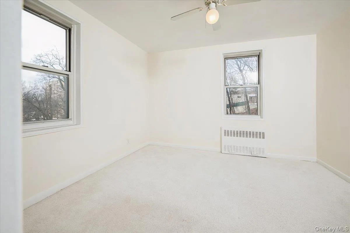 Unfurnished room featuring radiator, light carpet, and a ceiling fan Unfurnished room featuring radiator, light carpet, and a ceiling fan