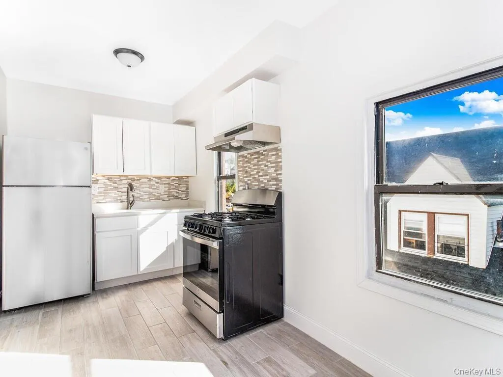 Kitchen featuring light countertops, freestanding refrigerator, gas stove, white cabinets, and under cabinet range hood Kitchen featuring light countertops, freestanding refrigerator, gas stove, white cabinets, and under cabinet range hood
