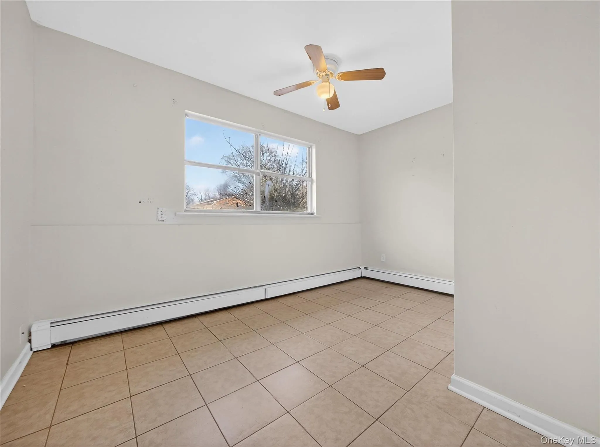 Empty room featuring baseboard heating, light tile patterned floors, and a ceiling fan Empty room featuring baseboard heating, light tile patterned floors, and a ceiling fan