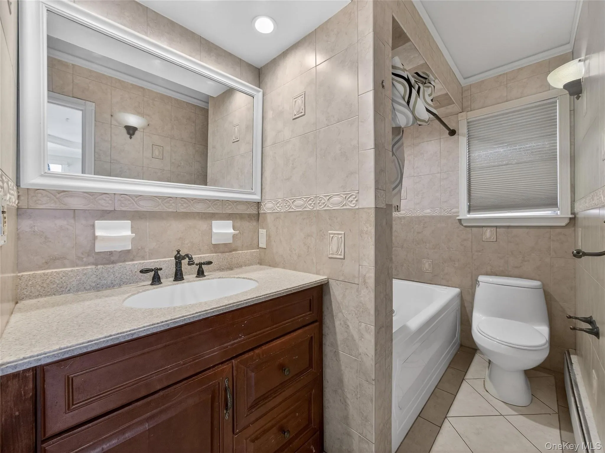 Bathroom with tile walls, vanity, a baseboard heating unit, light tile patterned floors, and shower / bath combination Bathroom with tile walls, vanity, a baseboard heating unit, light tile patterned floors, and shower / bath combination