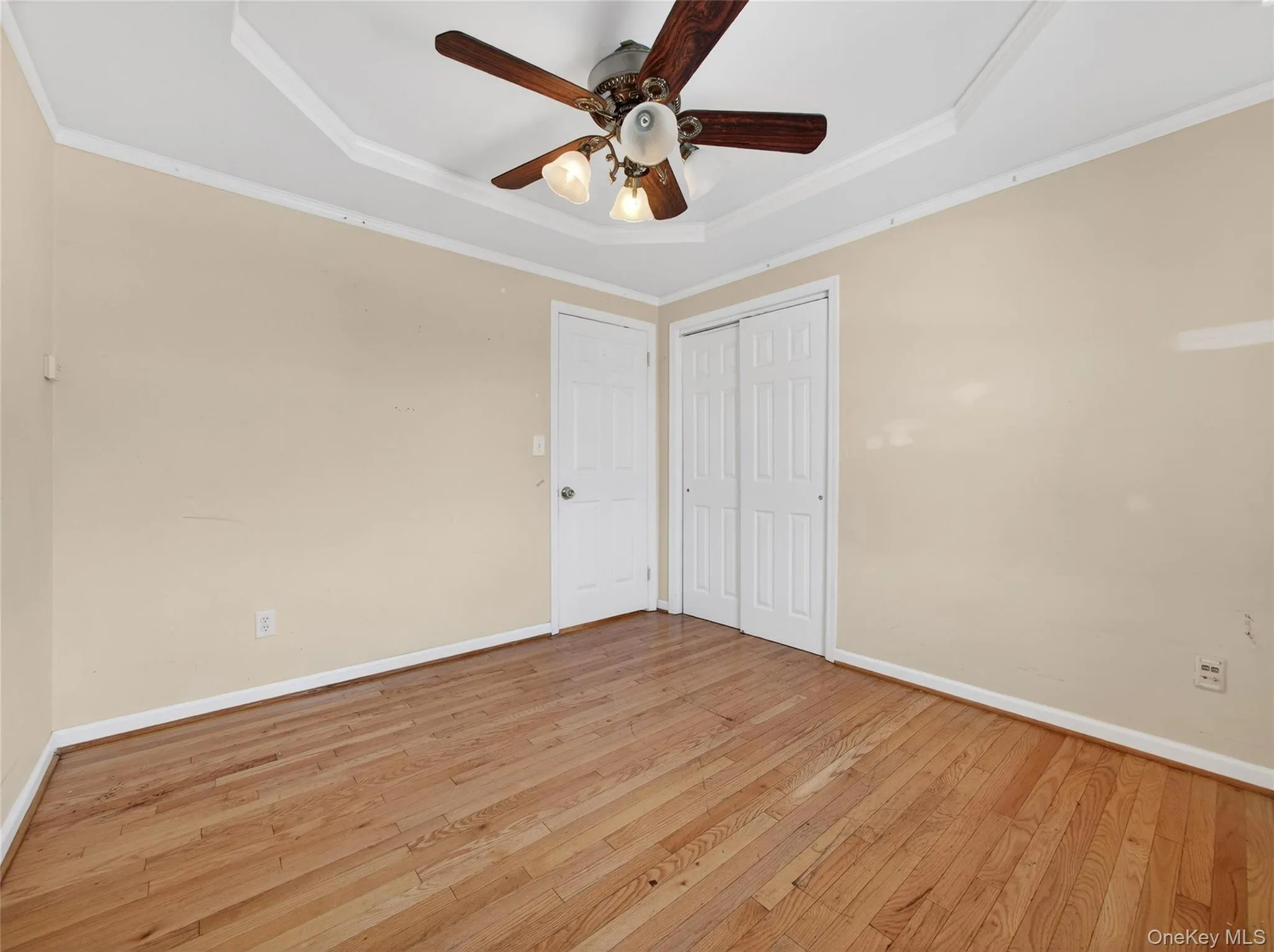 Unfurnished bedroom featuring a raised ceiling, wood-type flooring, ornamental molding, ceiling fan, and a closet Unfurnished bedroom featuring a raised ceiling, wood-type flooring, ornamental molding, ceiling fan, and a closet