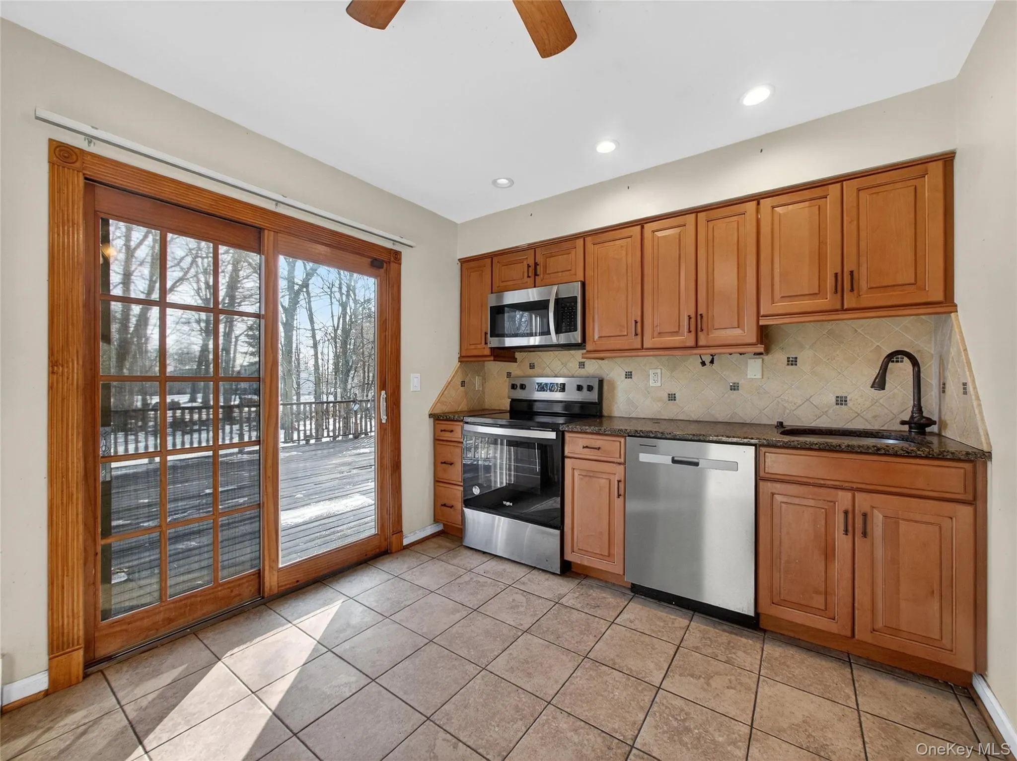 Kitchen with stainless steel appliances, brown cabinetry, dark stone countertops, recessed lighting, and decorative backsplash Kitchen with stainless steel appliances, brown cabinetry, dark stone countertops, recessed lighting, and decorative backsplash