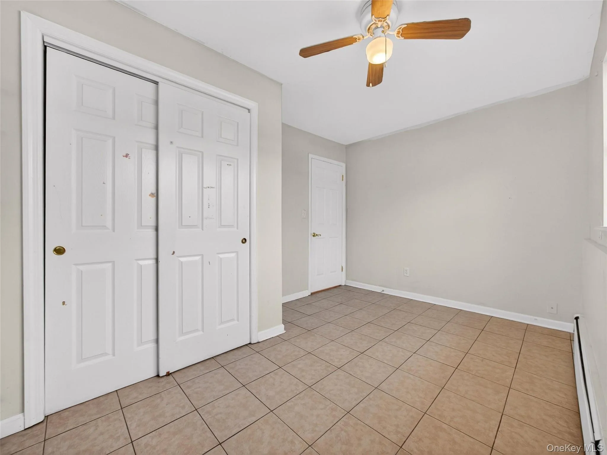 Unfurnished bedroom with a baseboard radiator, a ceiling fan, a closet, and light tile patterned floors Unfurnished bedroom with a baseboard radiator, a ceiling fan, a closet, and light tile patterned floors