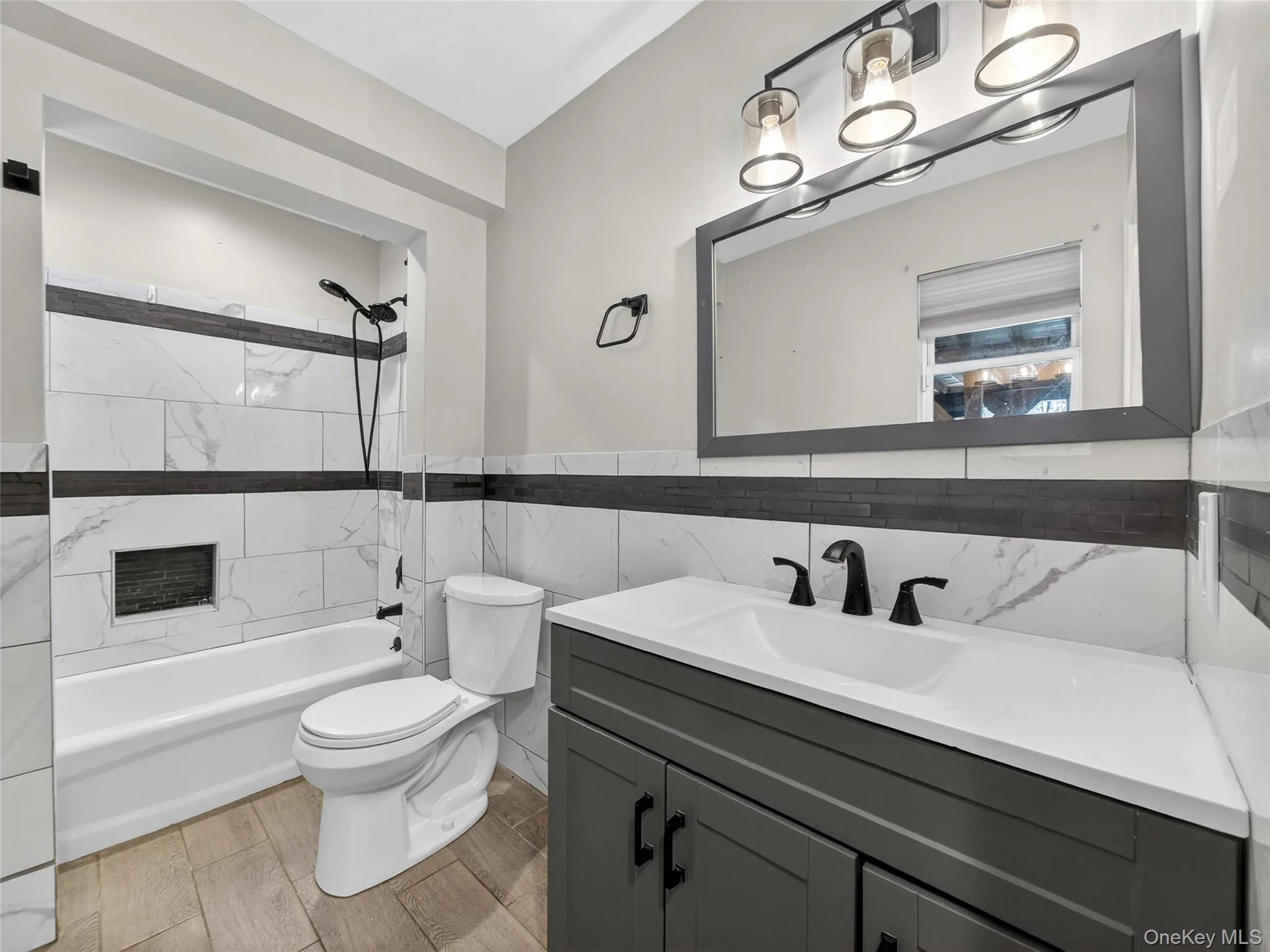 Full bath with vanity, shower / bathtub combination, tile walls, a wainscoted wall, and wood finish floors Full bath with vanity, shower / bathtub combination, tile walls, a wainscoted wall, and wood finish floors