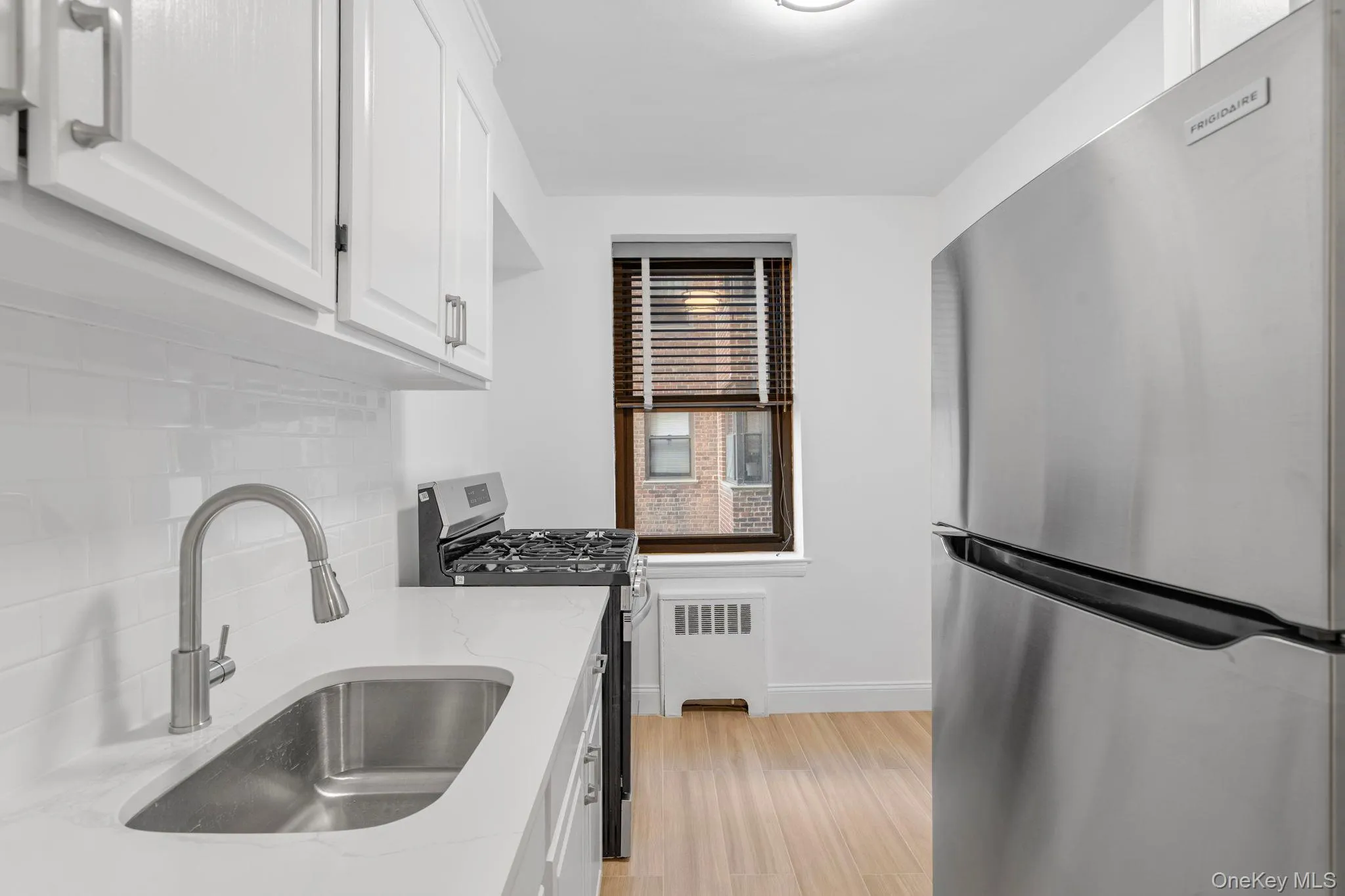 Kitchen with stainless steel appliances, radiator heating unit, white cabinetry, light stone countertops, and light wood flooring Kitchen with stainless steel appliances, radiator heating unit, white cabinetry, light stone countertops, and light wood flooring