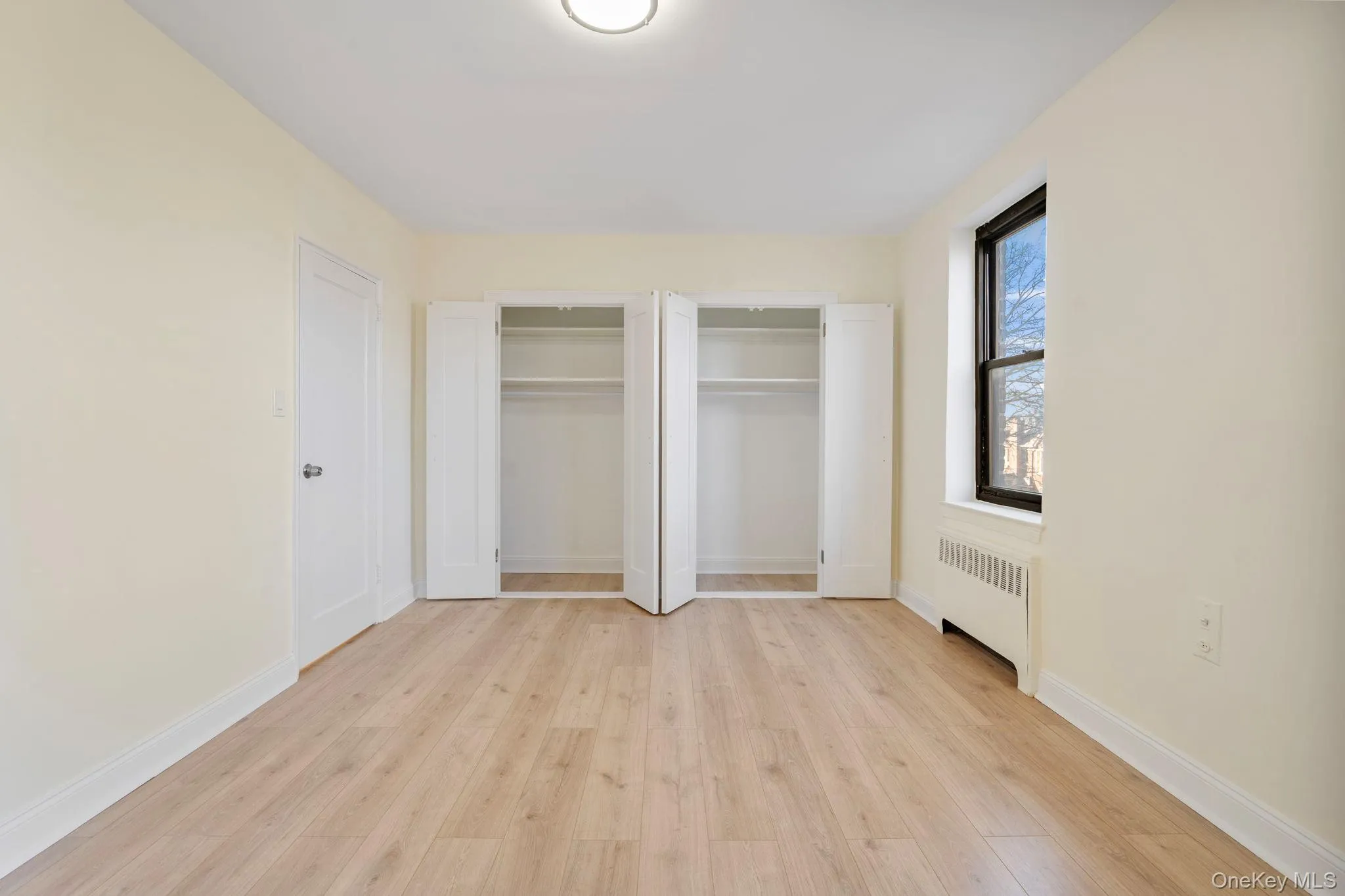 Bedroom with light wood flooring, radiator, and two closets Bedroom with light wood flooring, radiator, and two closets