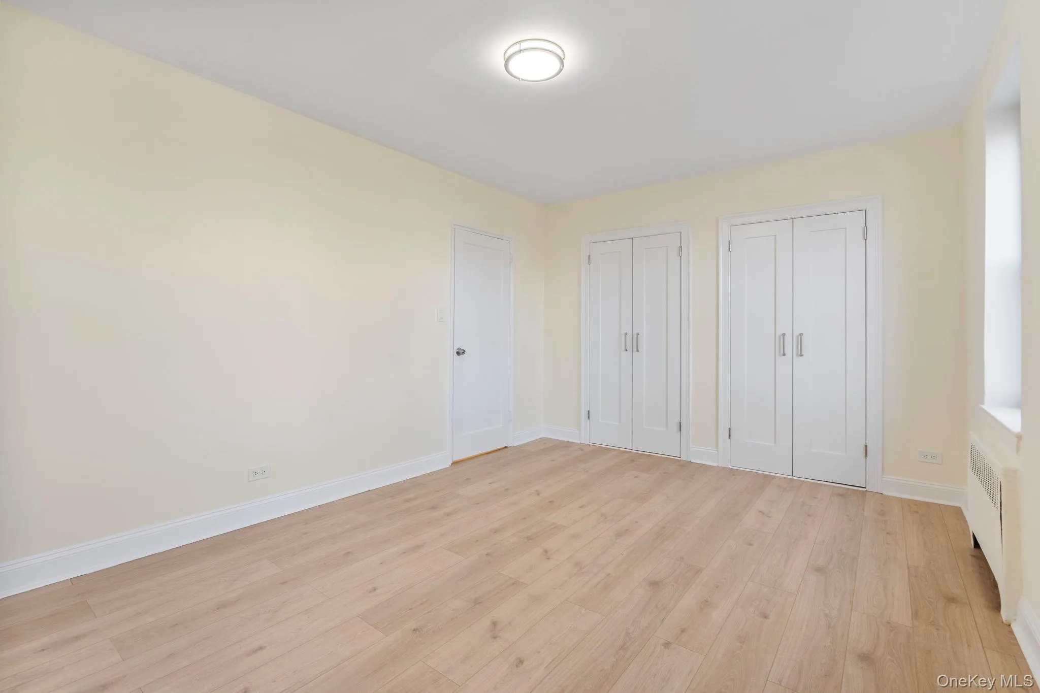 Bedroom featuring multiple closets, light wood floors, and radiator heating unit Bedroom featuring multiple closets, light wood floors, and radiator heating unit