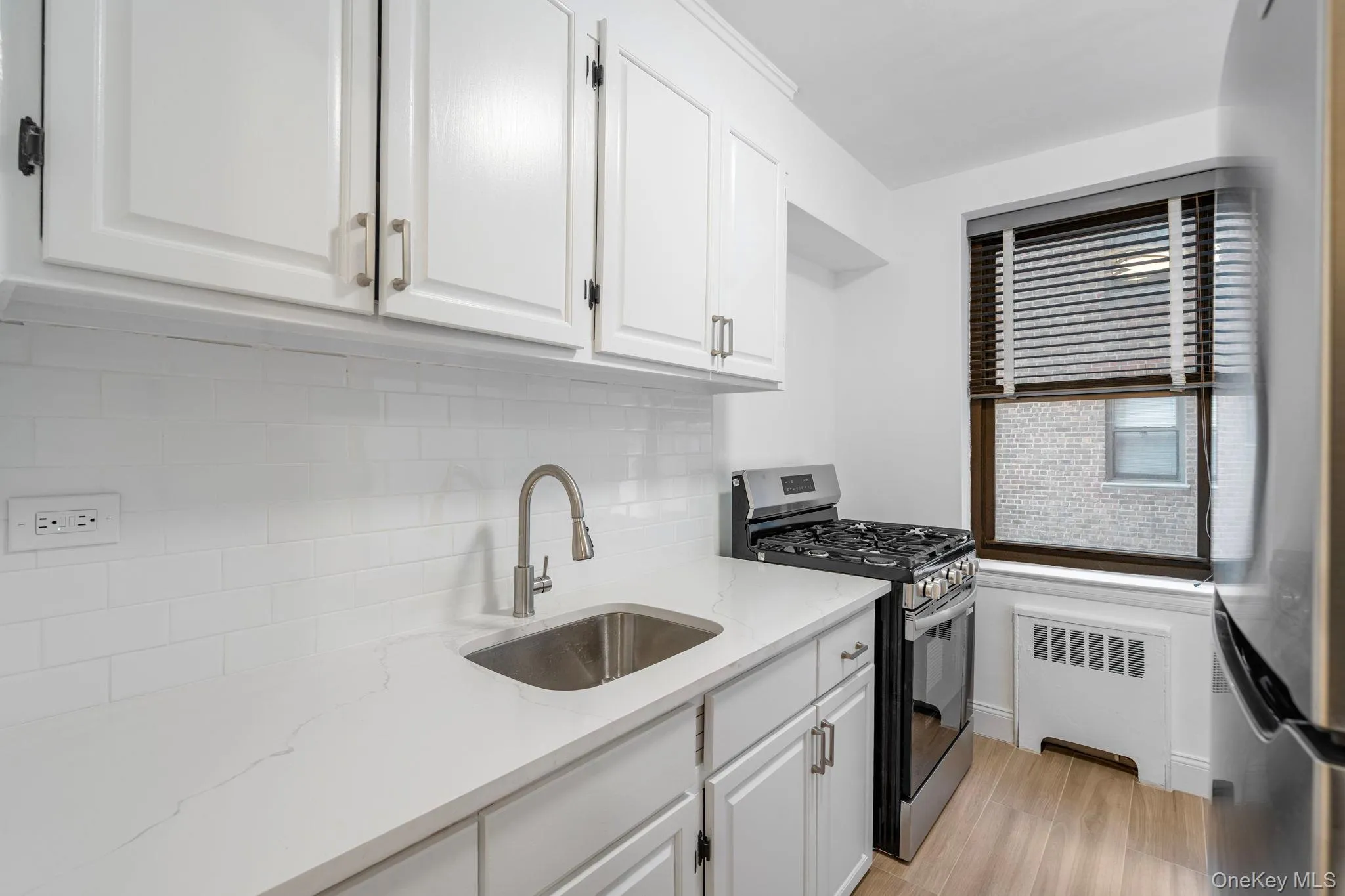 Kitchen with appliances with stainless steel finishes, white cabinets, radiator heating unit, light stone counters, and light wood finished floors Kitchen with appliances with stainless steel finishes, white cabinets, radiator heating unit, light stone counters, and light wood finished floors