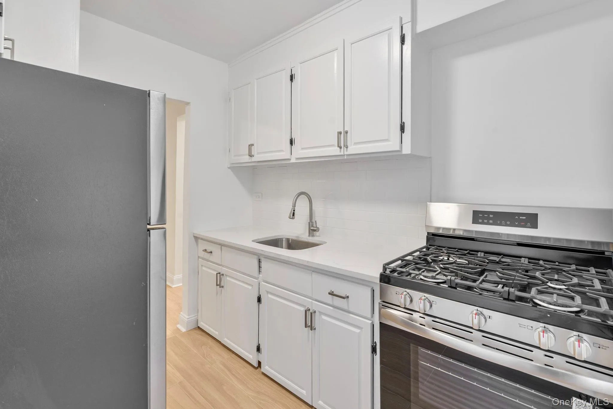 Kitchen with appliances with stainless steel finishes, white cabinets, light stone countertops, decorative backsplash, and light wood flooring Kitchen with appliances with stainless steel finishes, white cabinets, light stone countertops, decorative backsplash, and light wood flooring