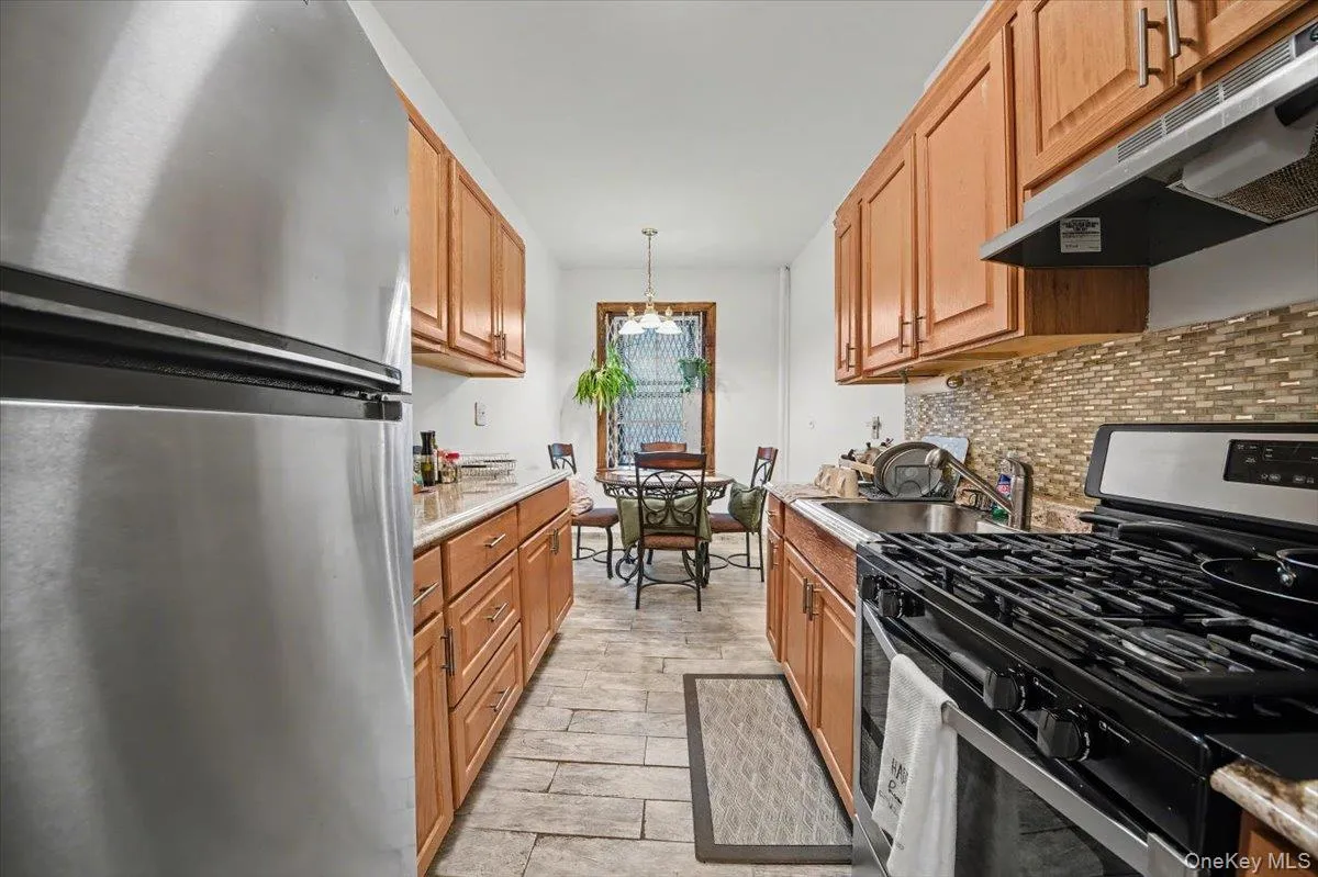 Kitchen with stainless steel appliances, ventilation hood, hanging light fixtures, a chandelier, and brown cabinetry Kitchen with stainless steel appliances, ventilation hood, hanging light fixtures, a chandelier, and brown cabinetry