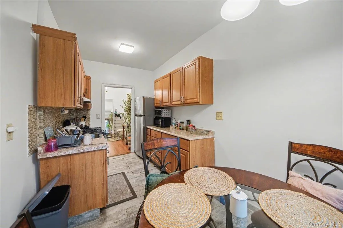 Kitchen featuring brown cabinets, appliances with stainless steel finishes, light wood-type flooring, decorative backsplash, and light stone counters Kitchen featuring brown cabinets, appliances with stainless steel finishes, light wood-type flooring, decorative backsplash, and light stone counters