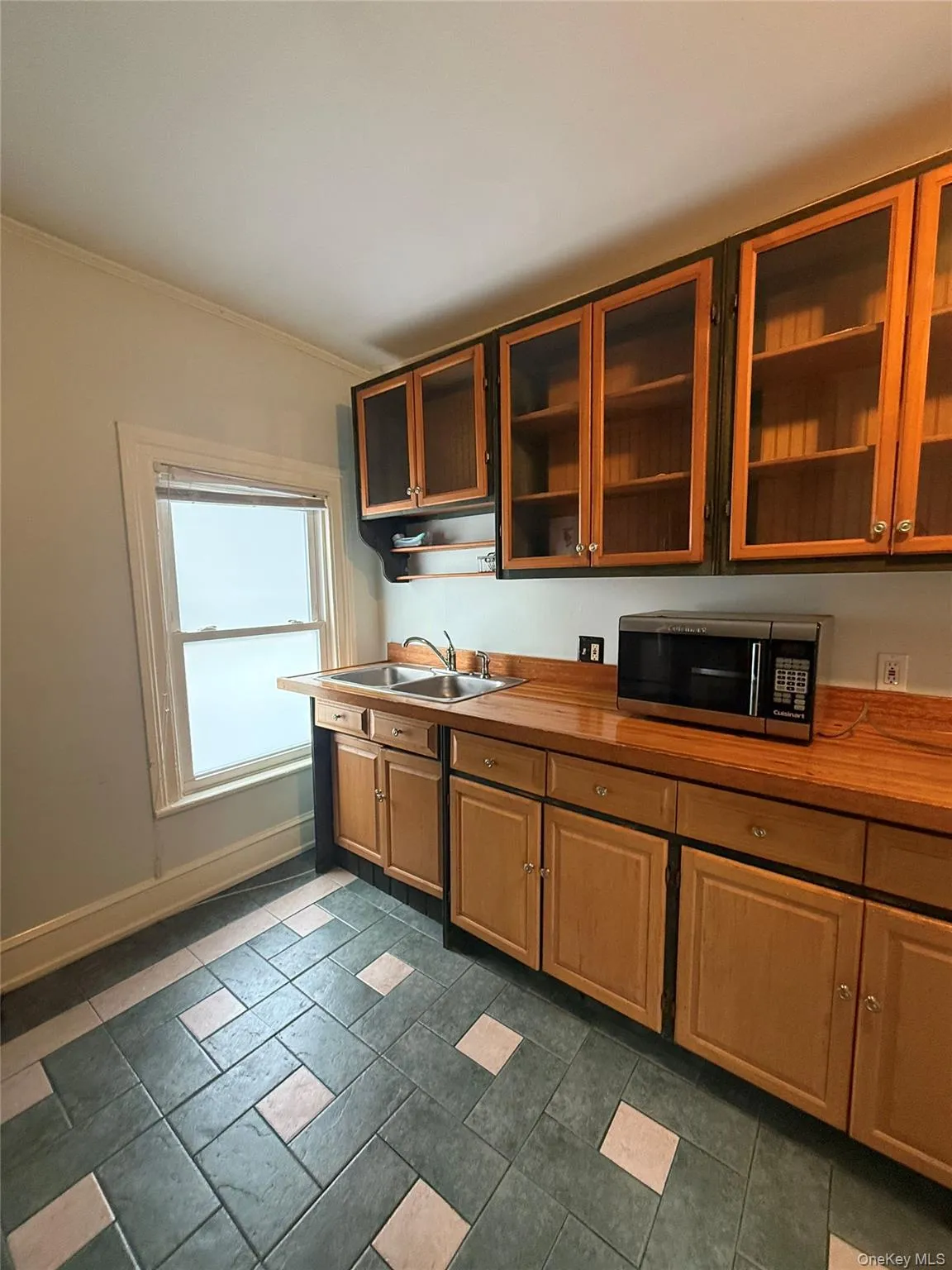 Kitchen featuring stainless steel microwave, glass insert cabinets, crown molding, butcher block countertops, and brown cabinets Kitchen featuring stainless steel microwave, glass insert cabinets, crown molding, butcher block countertops, and brown cabinets