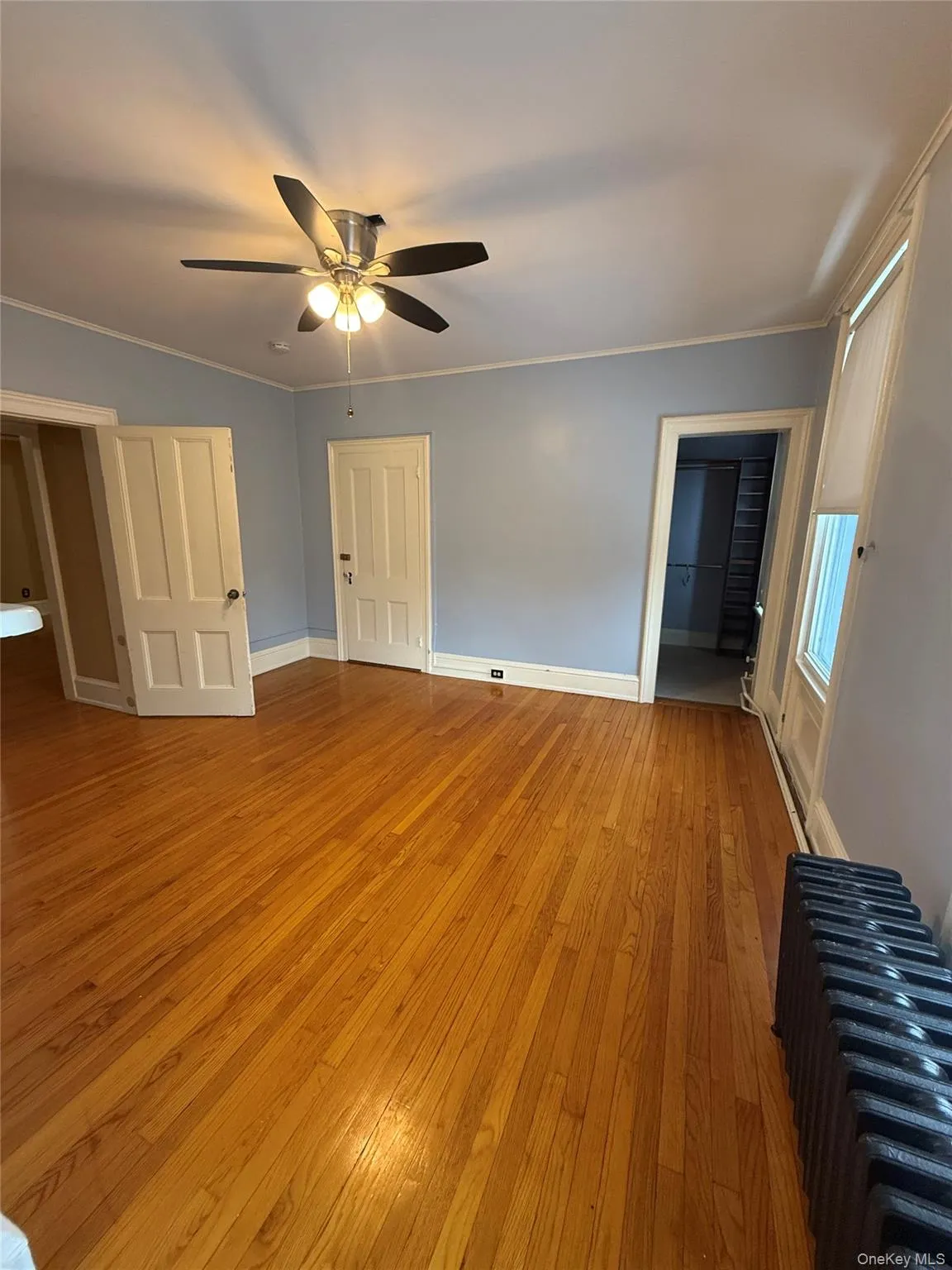 Unfurnished bedroom with crown molding, light wood-style flooring, radiator, and a ceiling fan Unfurnished bedroom with crown molding, light wood-style flooring, radiator, and a ceiling fan