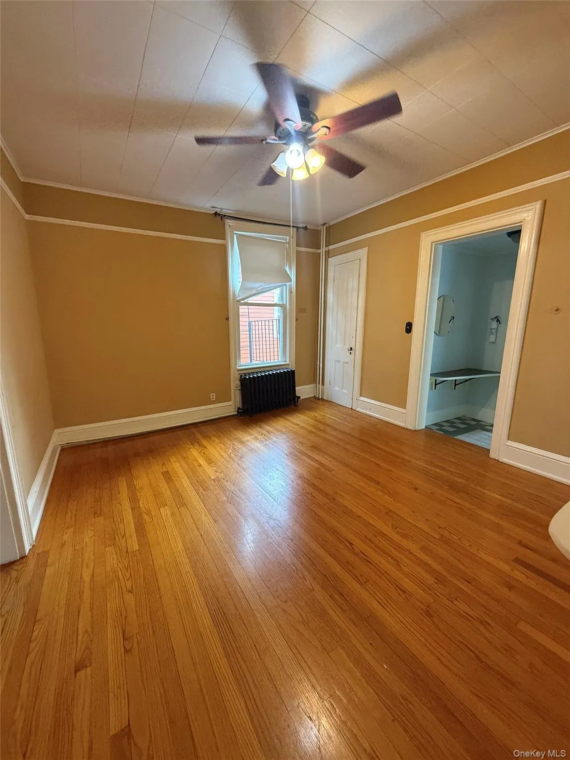 Unfurnished bedroom featuring radiator, light wood finished floors, crown molding, and ceiling fan Unfurnished bedroom featuring radiator, light wood finished floors, crown molding, and ceiling fan