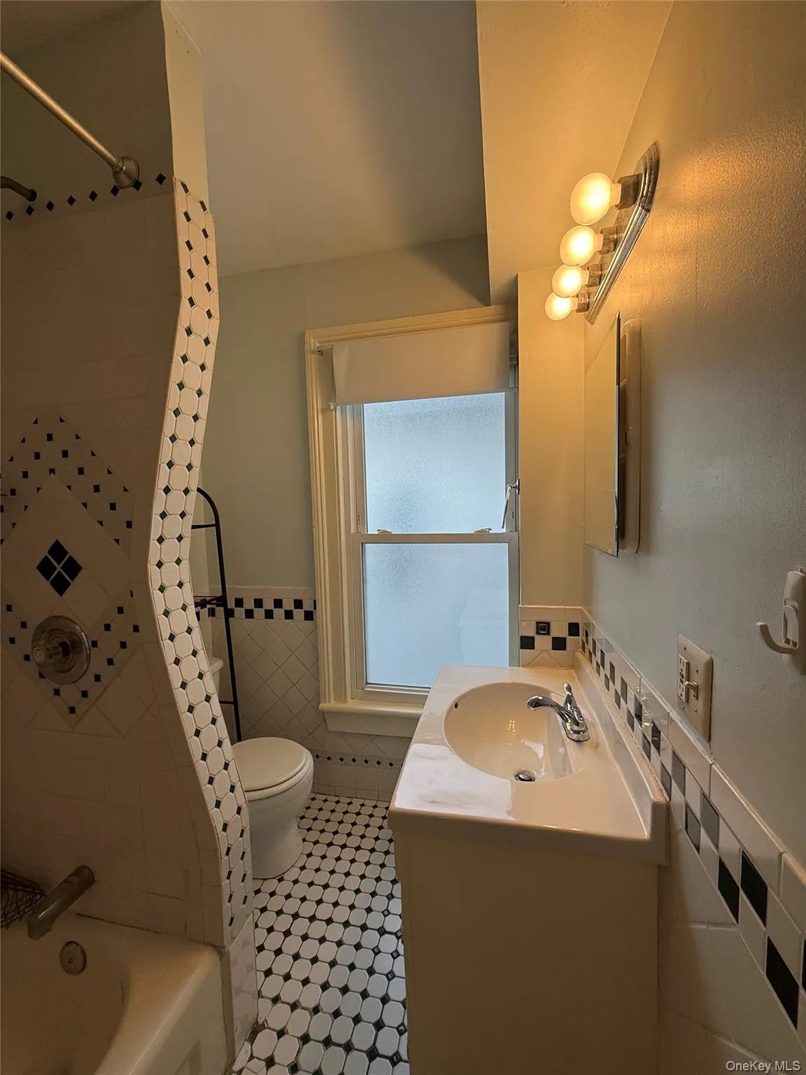 Full bathroom with vanity, wainscoting, washtub / shower combination, and tile walls Full bathroom with vanity, wainscoting, washtub / shower combination, and tile walls