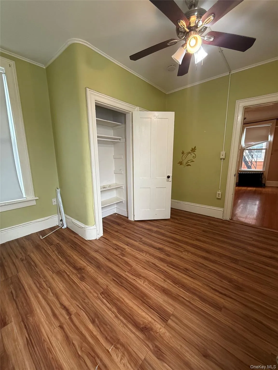 Unfurnished bedroom with ornamental molding, wood finished floors, ceiling fan, and a closet Unfurnished bedroom with ornamental molding, wood finished floors, ceiling fan, and a closet
