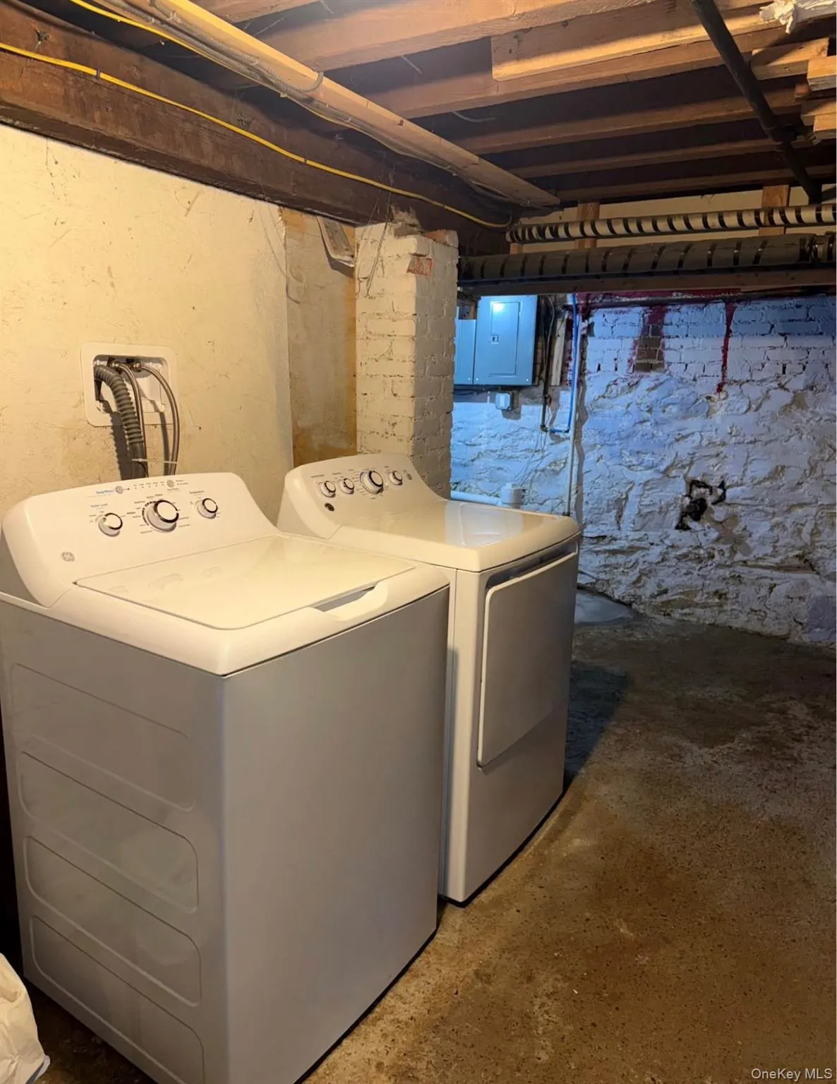 Washroom featuring unfinished concrete flooring, electric panel, and washing machine and clothes dryer Washroom featuring unfinished concrete flooring, electric panel, and washing machine and clothes dryer
