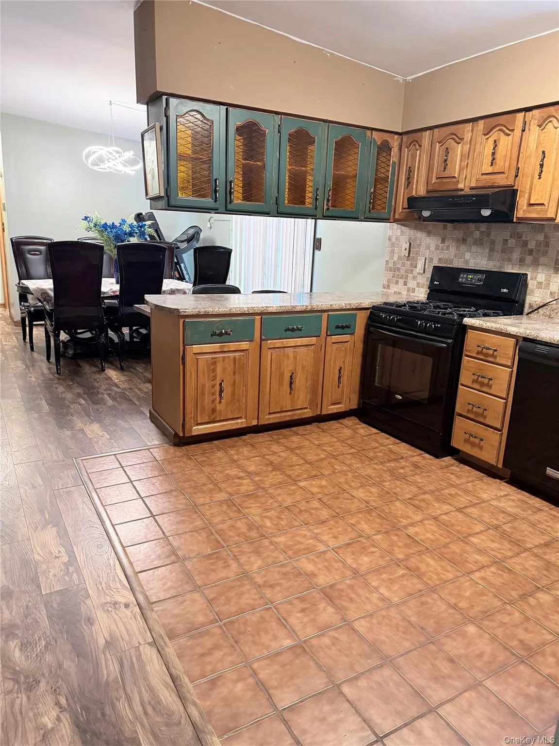 Kitchen featuring a peninsula, black appliances, glass insert cabinets, brown cabinetry, and under cabinet range hood Kitchen featuring a peninsula, black appliances, glass insert cabinets, brown cabinetry, and under cabinet range hood