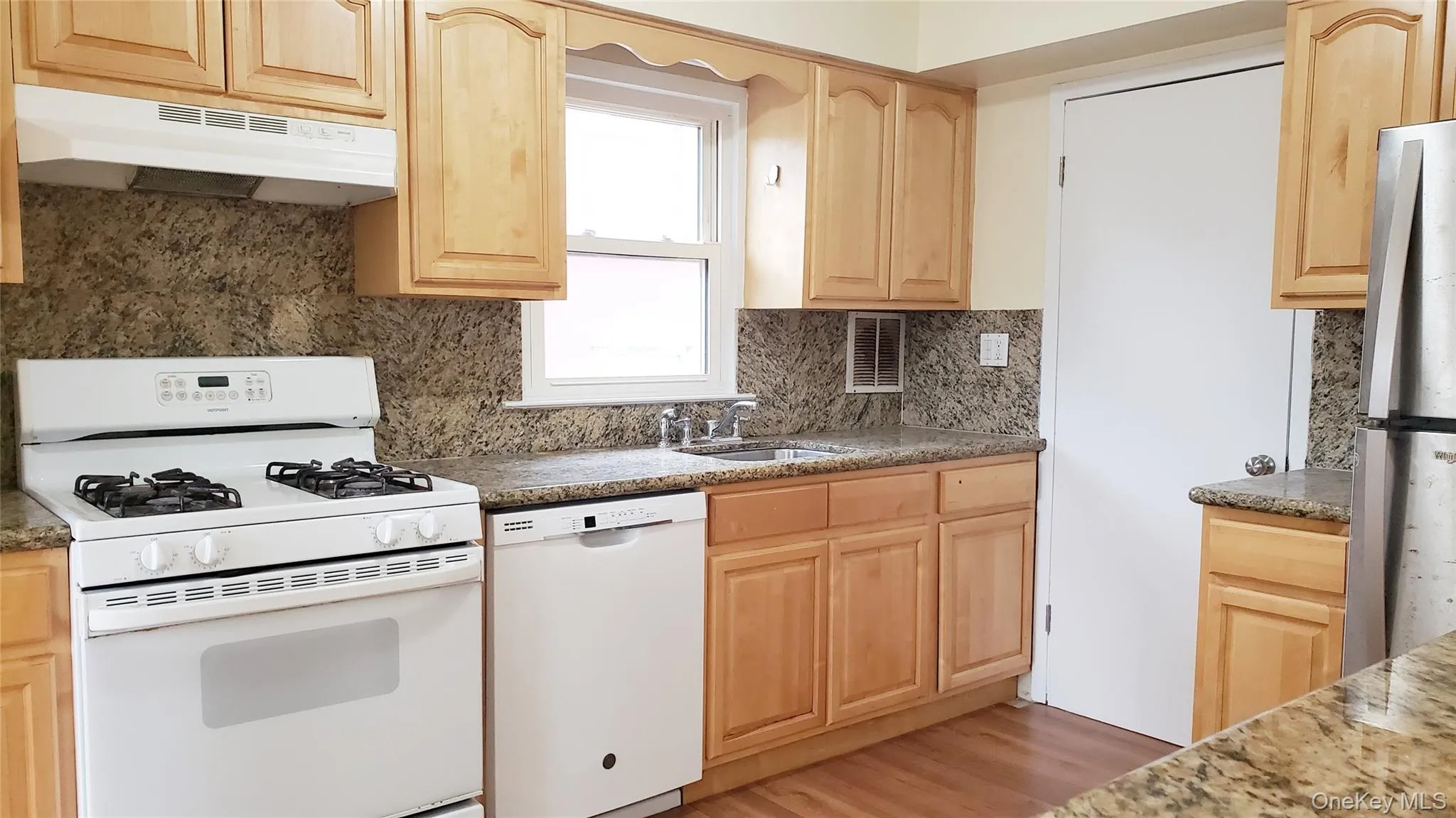 Kitchen featuring light brown cabinetry, white appliances, under cabinet range hood, light wood finished floors, and decorative backsplash Kitchen featuring light brown cabinetry, white appliances, under cabinet range hood, light wood finished floors, and decorative backsplash