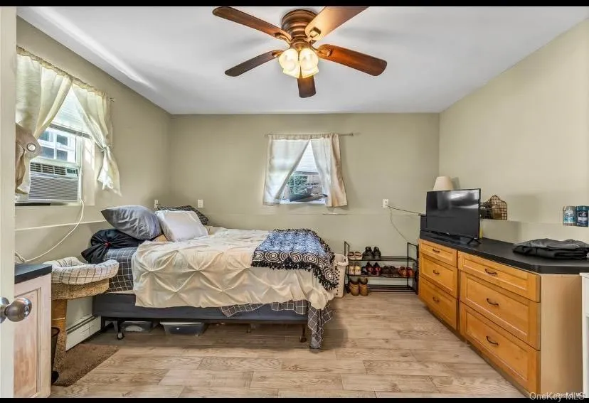 Bedroom featuring multiple windows, light wood-style flooring, a baseboard radiator, and ceiling fan Bedroom featuring multiple windows, light wood-style flooring, a baseboard radiator, and ceiling fan