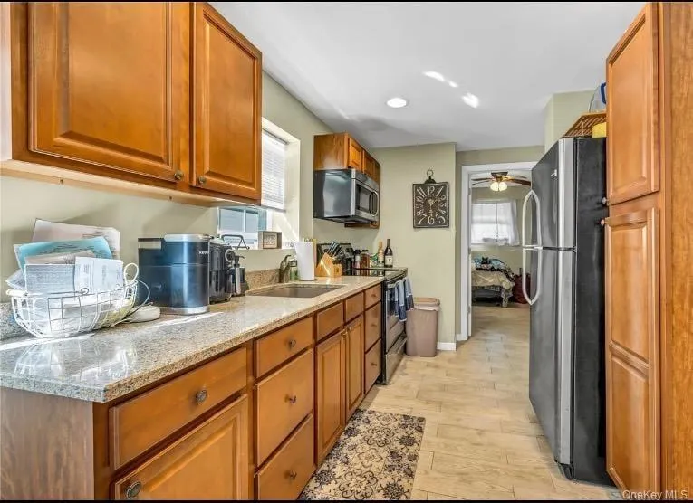 Kitchen featuring brown cabinets, appliances with stainless steel finishes, light stone countertops, plenty of natural light, and recessed lighting Kitchen featuring brown cabinets, appliances with stainless steel finishes, light stone countertops, plenty of natural light, and recessed lighting