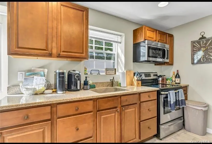 Kitchen with brown cabinetry, appliances with stainless steel finishes, and light stone countertops Kitchen with brown cabinetry, appliances with stainless steel finishes, and light stone countertops