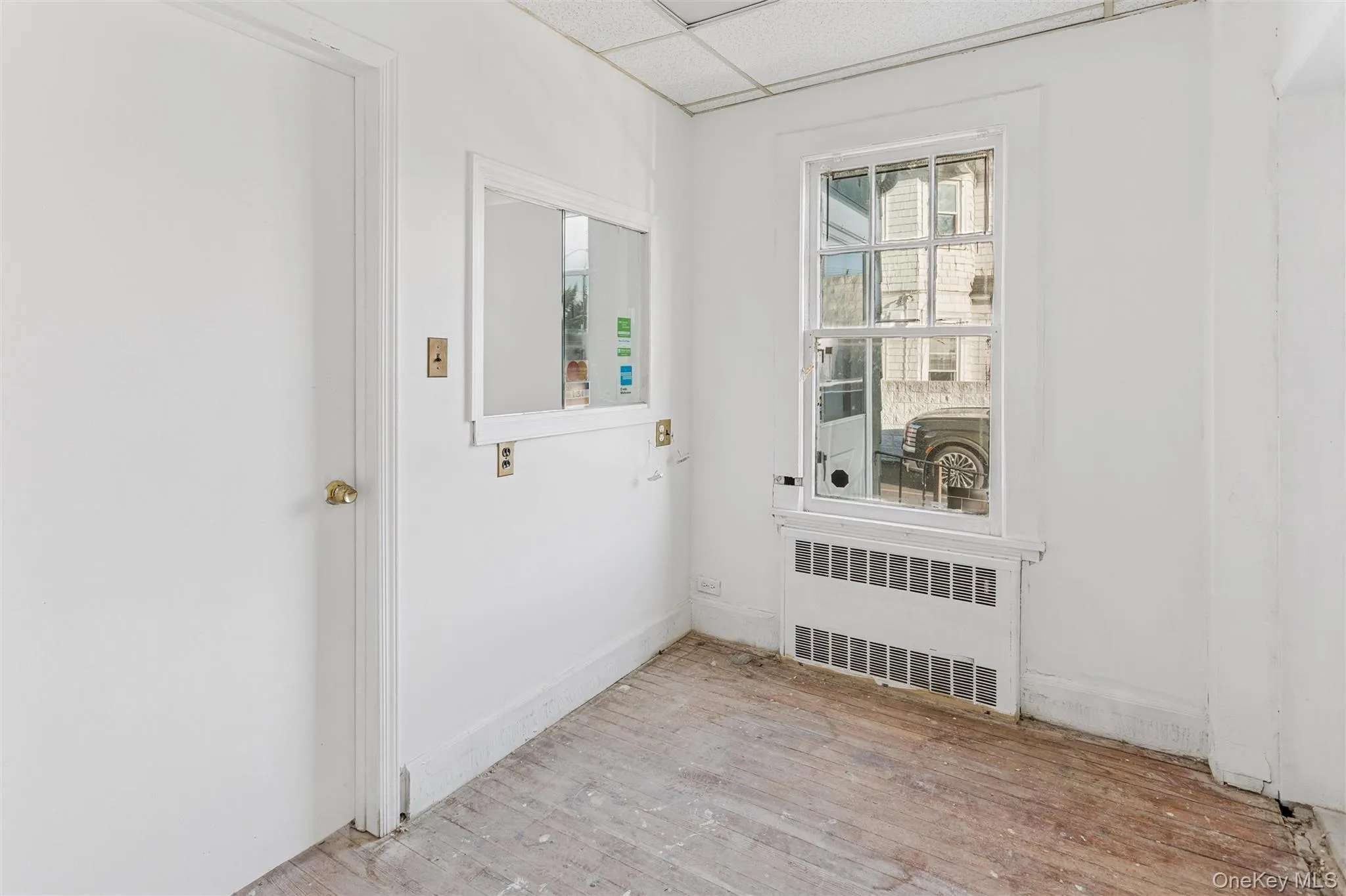 Empty room with radiator heating unit, a paneled ceiling, and light wood-style flooring Empty room with radiator heating unit, a paneled ceiling, and light wood-style flooring