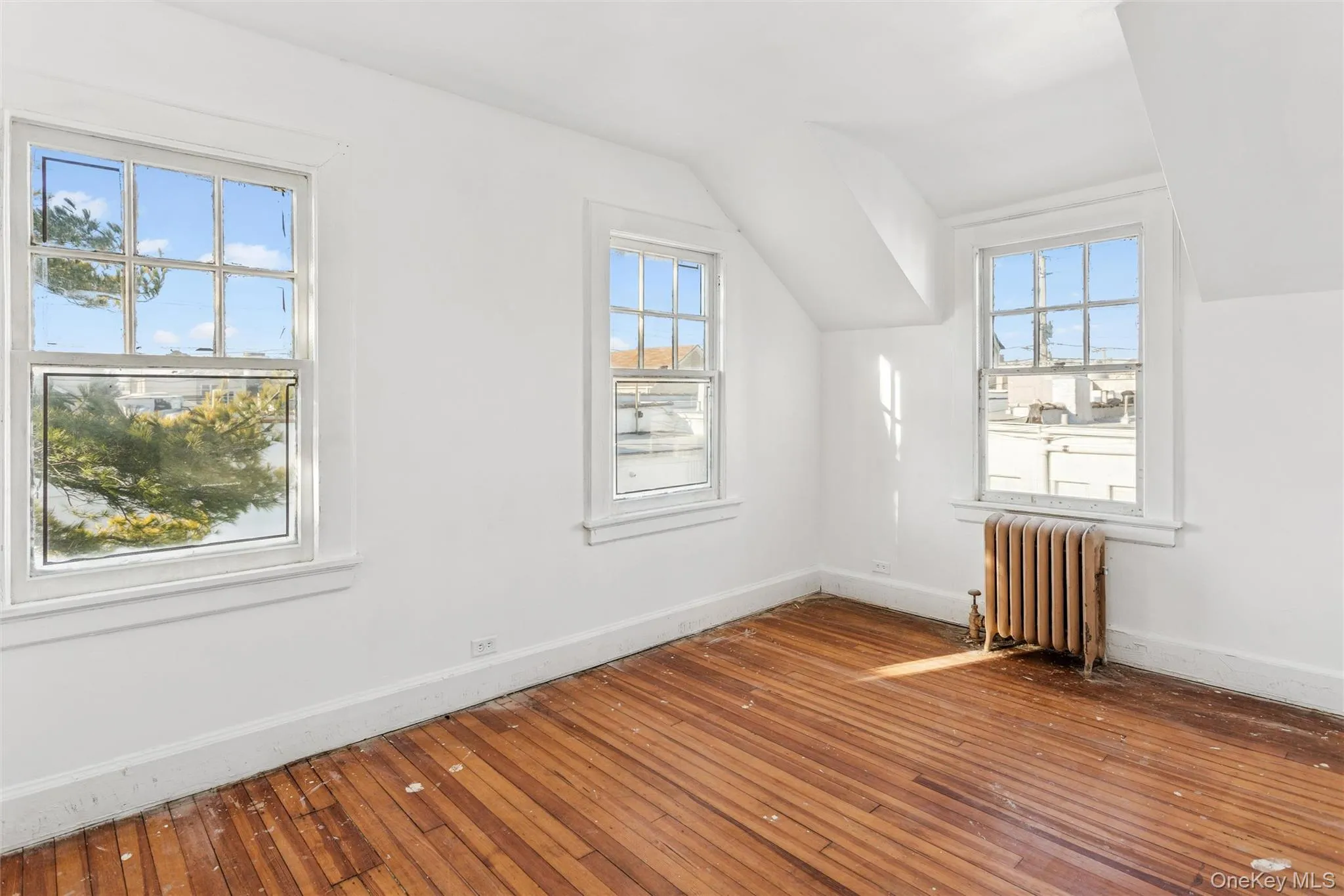 Additional living space featuring radiator, wood-type flooring, healthy amount of natural light, and vaulted ceiling Additional living space featuring radiator, wood-type flooring, healthy amount of natural light, and vaulted ceiling