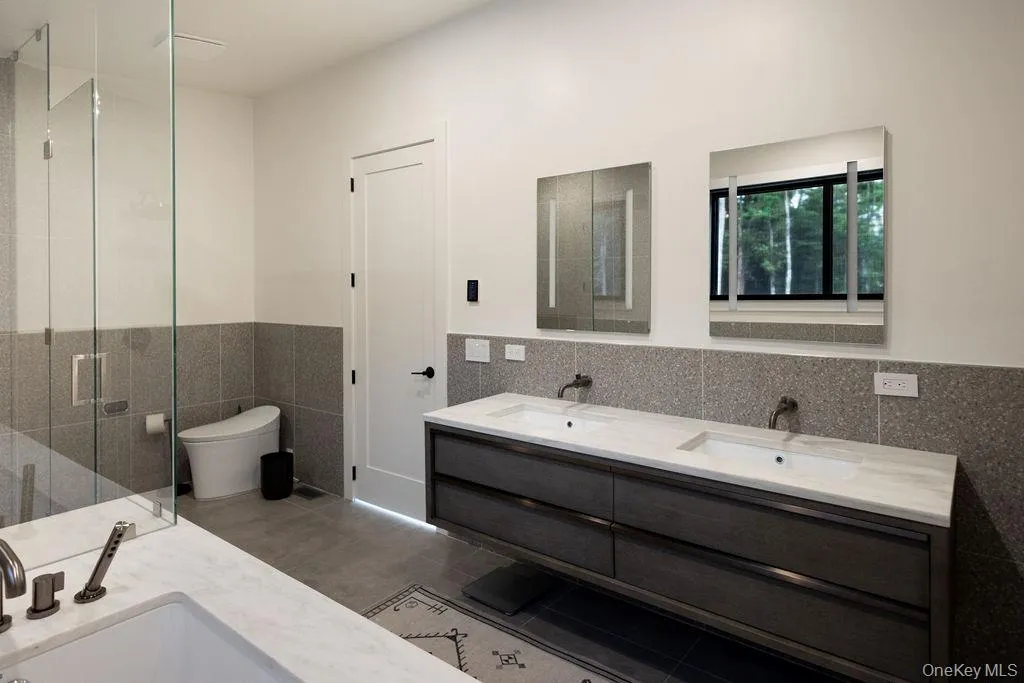 Full bath with tile walls, double vanity, a wainscoted wall, a stall shower, and dark tile patterned floors Full bath with tile walls, double vanity, a wainscoted wall, a stall shower, and dark tile patterned floors