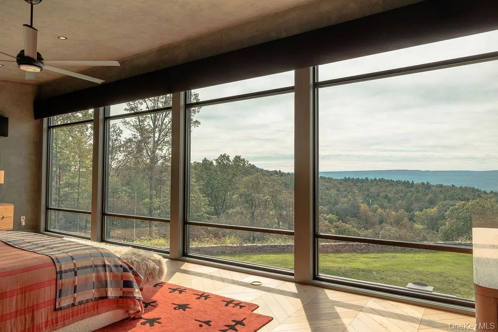 Bedroom featuring floor to ceiling windows, a wooded view, and a ceiling fan Bedroom featuring floor to ceiling windows, a wooded view, and a ceiling fan