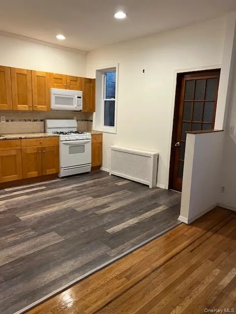 Kitchen with brown cabinets, white appliances, dark wood-style flooring, radiator, and recessed lighting Kitchen with brown cabinets, white appliances, dark wood-style flooring, radiator, and recessed lighting