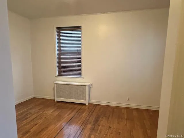 Spare room featuring radiator heating unit and wood finished floors Spare room featuring radiator heating unit and wood finished floors