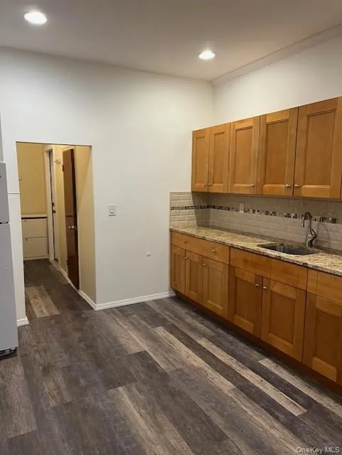 Kitchen with brown cabinetry, light stone countertops, tasteful backsplash, dark wood finished floors, and recessed lighting Kitchen with brown cabinetry, light stone countertops, tasteful backsplash, dark wood finished floors, and recessed lighting