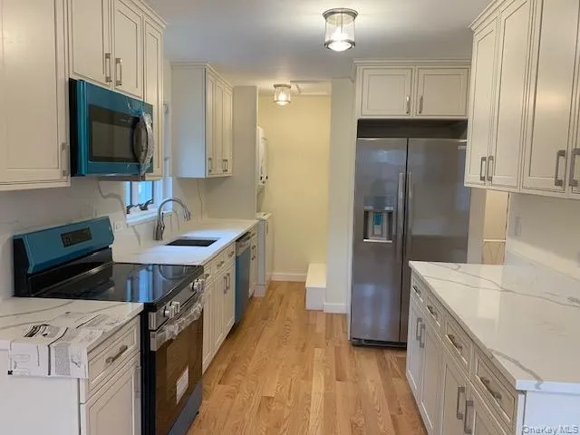 Kitchen featuring appliances with stainless steel finishes, light stone counters, light wood finished floors, and white cabinetry Kitchen featuring appliances with stainless steel finishes, light stone counters, light wood finished floors, and white cabinetry