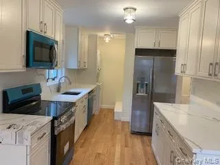 Kitchen featuring stainless steel appliances, light wood-type flooring, light stone countertops, and white cabinetry Kitchen featuring stainless steel appliances, light wood-type flooring, light stone countertops, and white cabinetry