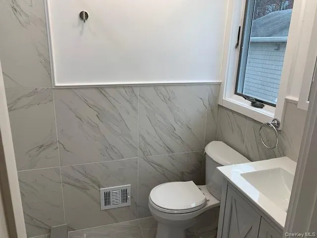 Bathroom featuring tile walls, vanity, and a wainscoted wall Bathroom featuring tile walls, vanity, and a wainscoted wall