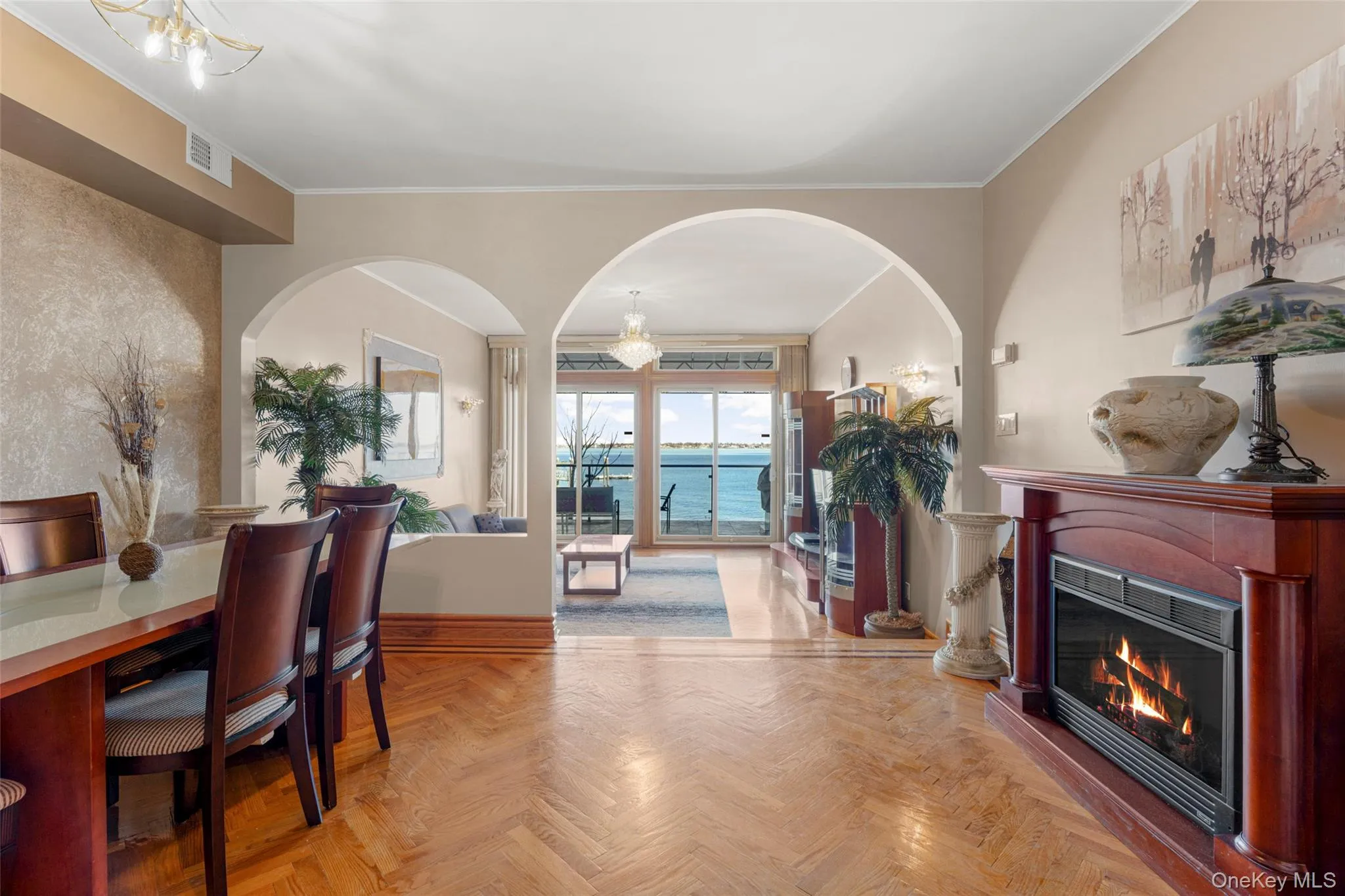 Dining room featuring arched walkways, a glass covered fireplace, ornamental molding, a chandelier, and a water view Dining room featuring arched walkways, a glass covered fireplace, ornamental molding, a chandelier, and a water view