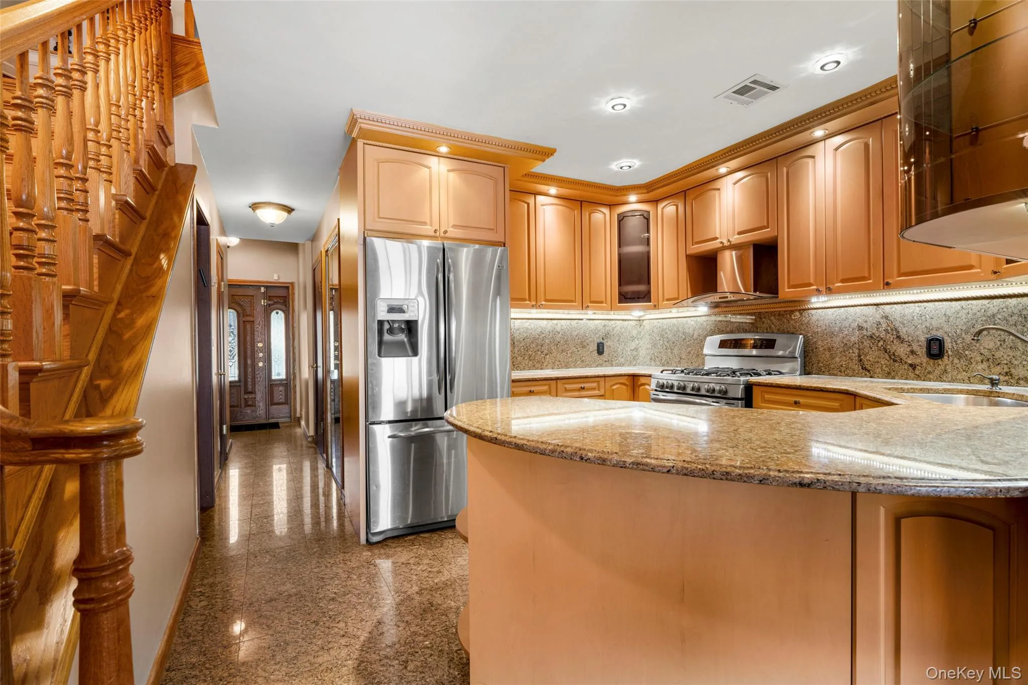 Kitchen with granite tiled floors, light stone countertops, appliances with stainless steel finishes, glass insert cabinets, and range hood Kitchen with granite tiled floors, light stone countertops, appliances with stainless steel finishes, glass insert cabinets, and range hood