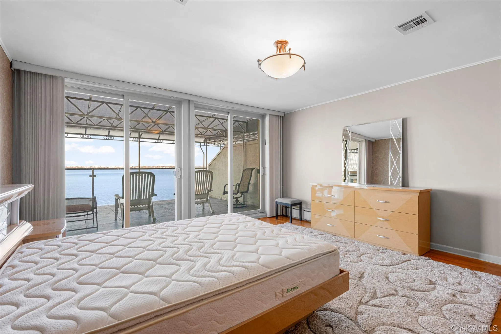 Bedroom featuring a water view, access to exterior, wood finished floors, a sunroom, and expansive windows Bedroom featuring a water view, access to exterior, wood finished floors, a sunroom, and expansive windows