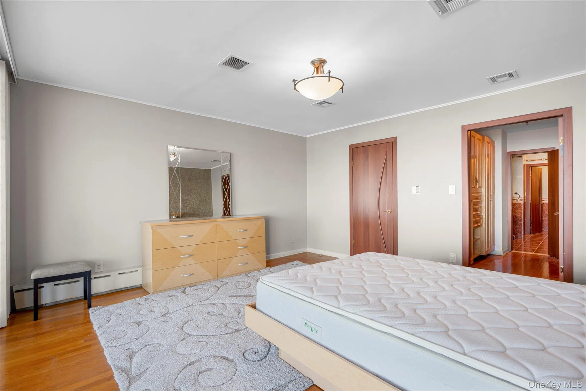 Bedroom featuring wood finished floors, a closet, a baseboard radiator, and crown molding Bedroom featuring wood finished floors, a closet, a baseboard radiator, and crown molding