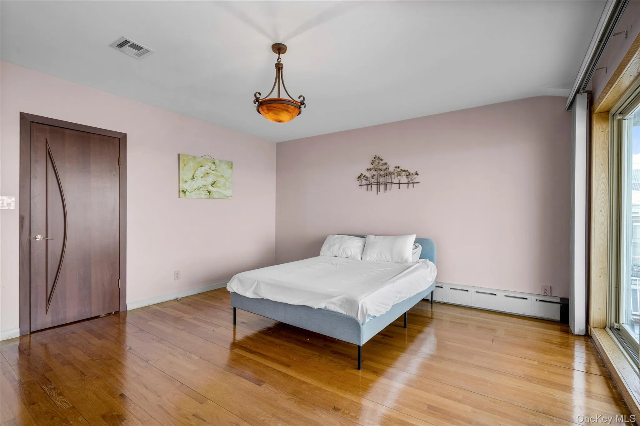 Bedroom featuring baseboard heating, wood-type flooring, and access to exterior Bedroom featuring baseboard heating, wood-type flooring, and access to exterior
