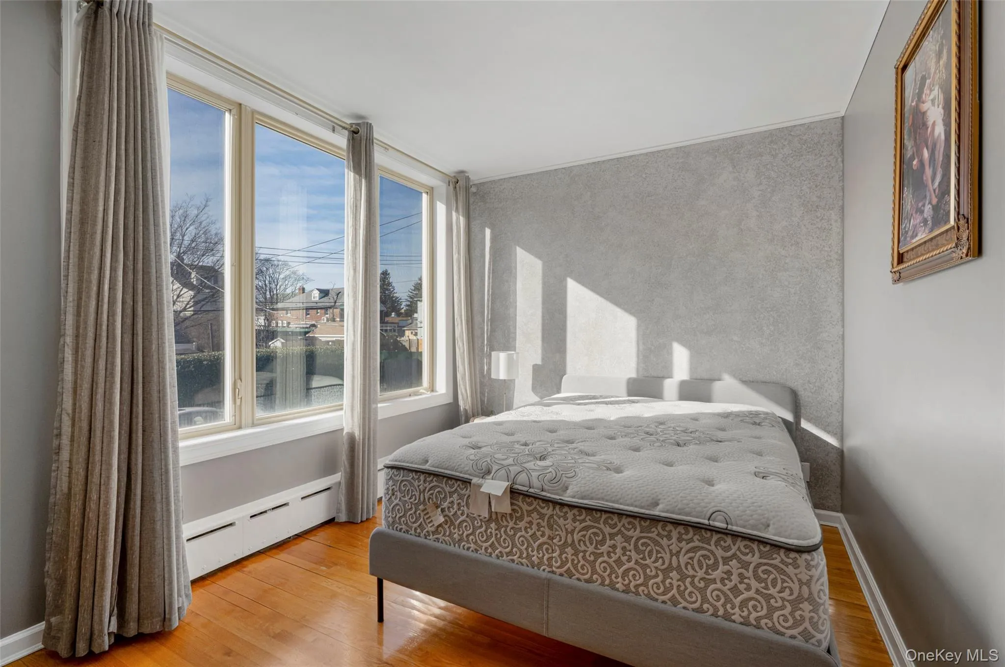 Bedroom featuring baseboard heating, wood finished floors, and an accent wall Bedroom featuring baseboard heating, wood finished floors, and an accent wall